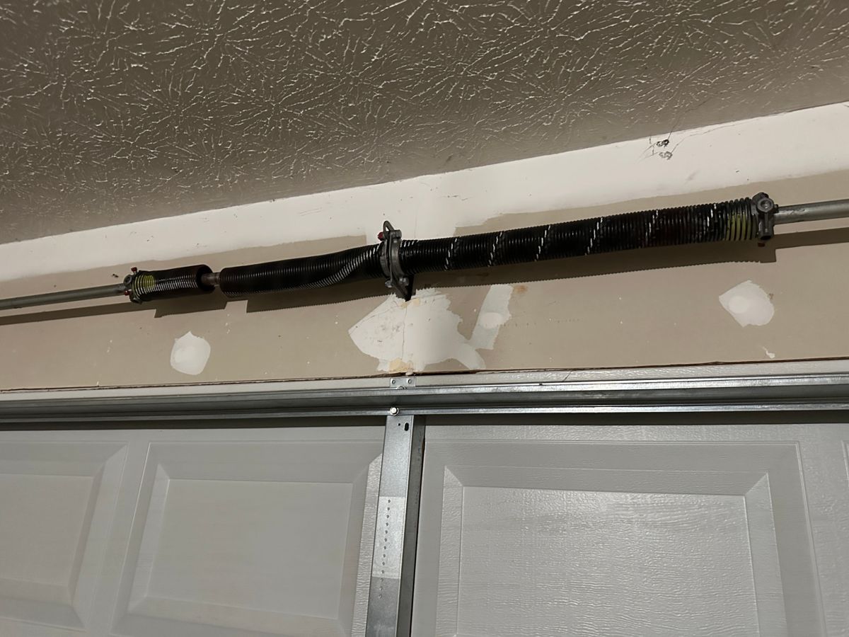 Broken garage door spring on the shaft above a residential garage door in Stone Mountain, Georgia, with the separated coils visible