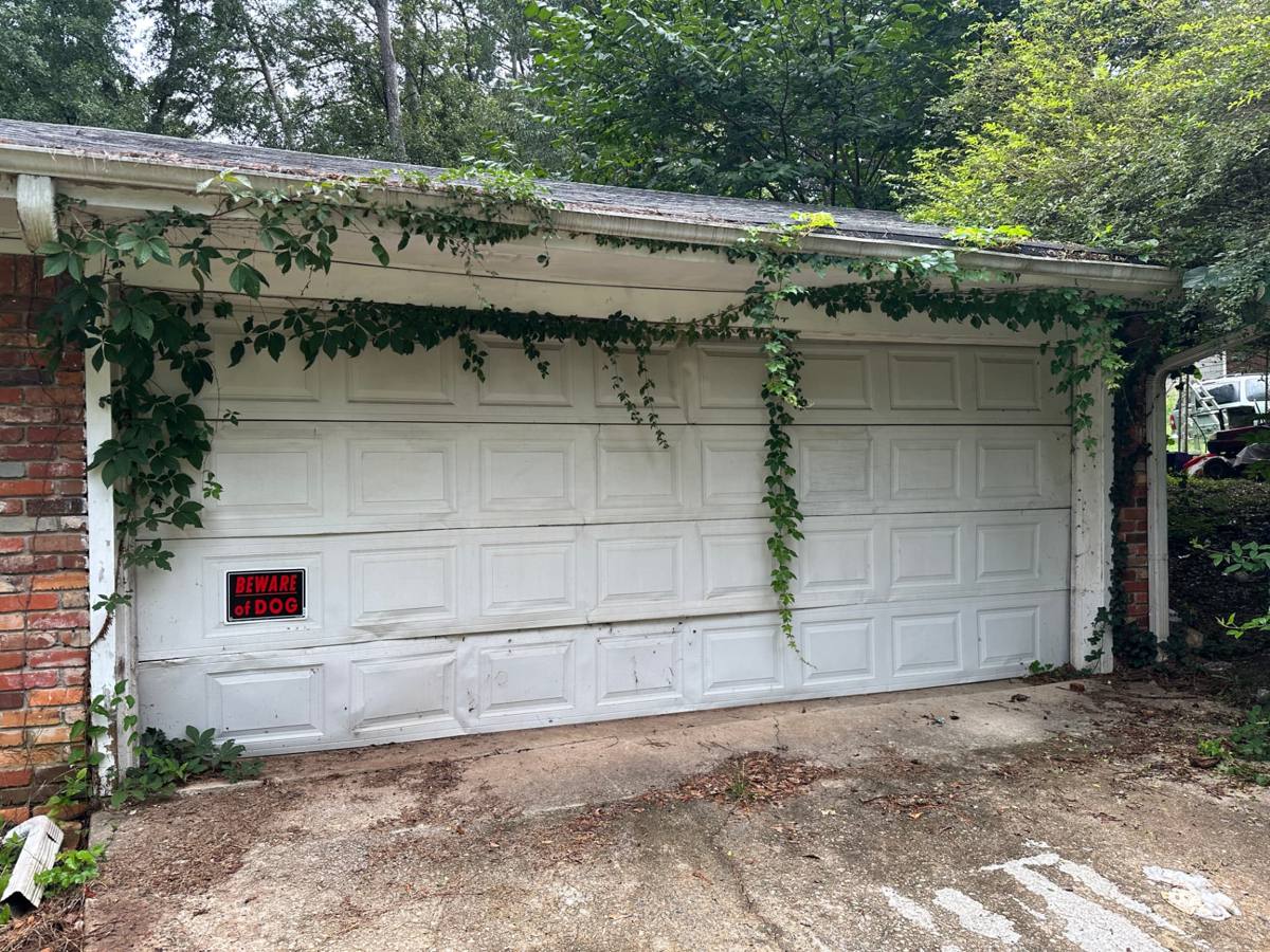 Damaged white garage door with buckled and creased lower panels on a Decatur, Georgia home