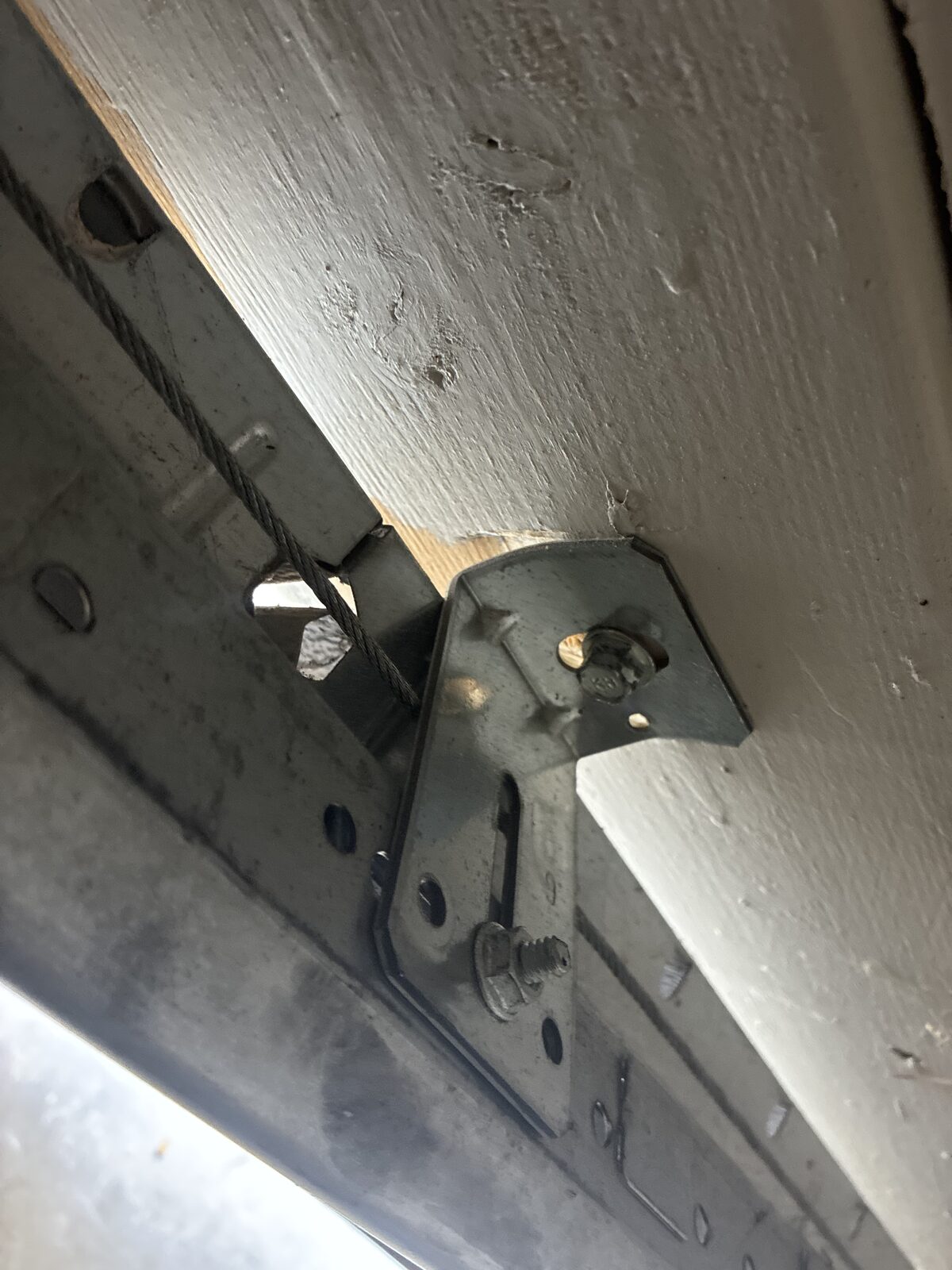 Damaged lift cable and track bracket on the off-track garage door before cable replacement in Decatur, Georgia