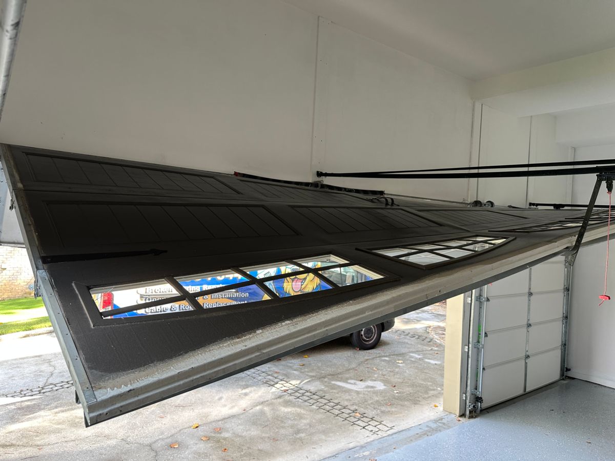 Severely damaged dark garage door hanging off its track at a steep angle inside an Atlanta, Georgia garage