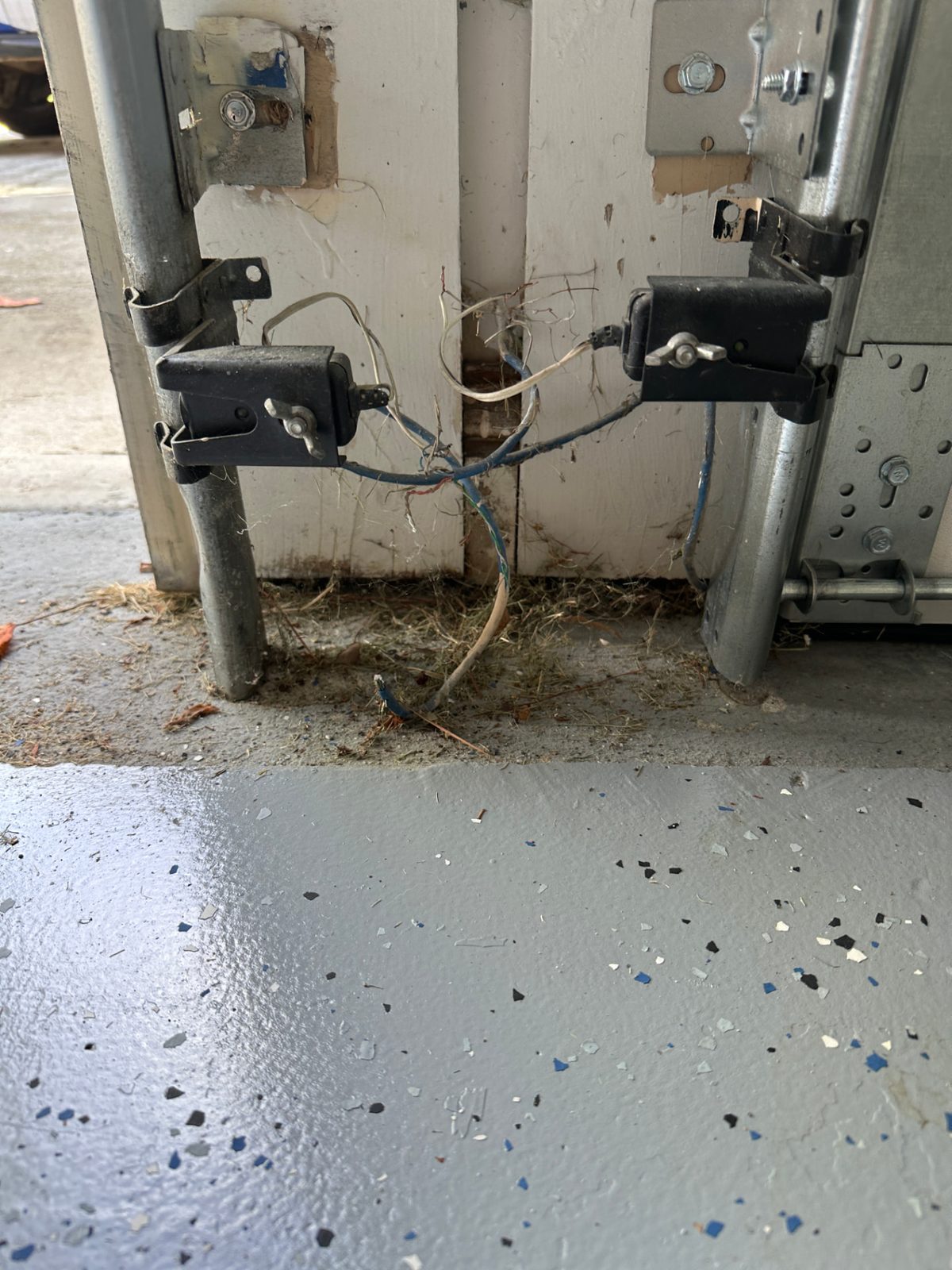 Garage door safety sensors at the bottom of the tracks with tangled, incorrectly connected wiring, repaired in Atlanta, Georgia