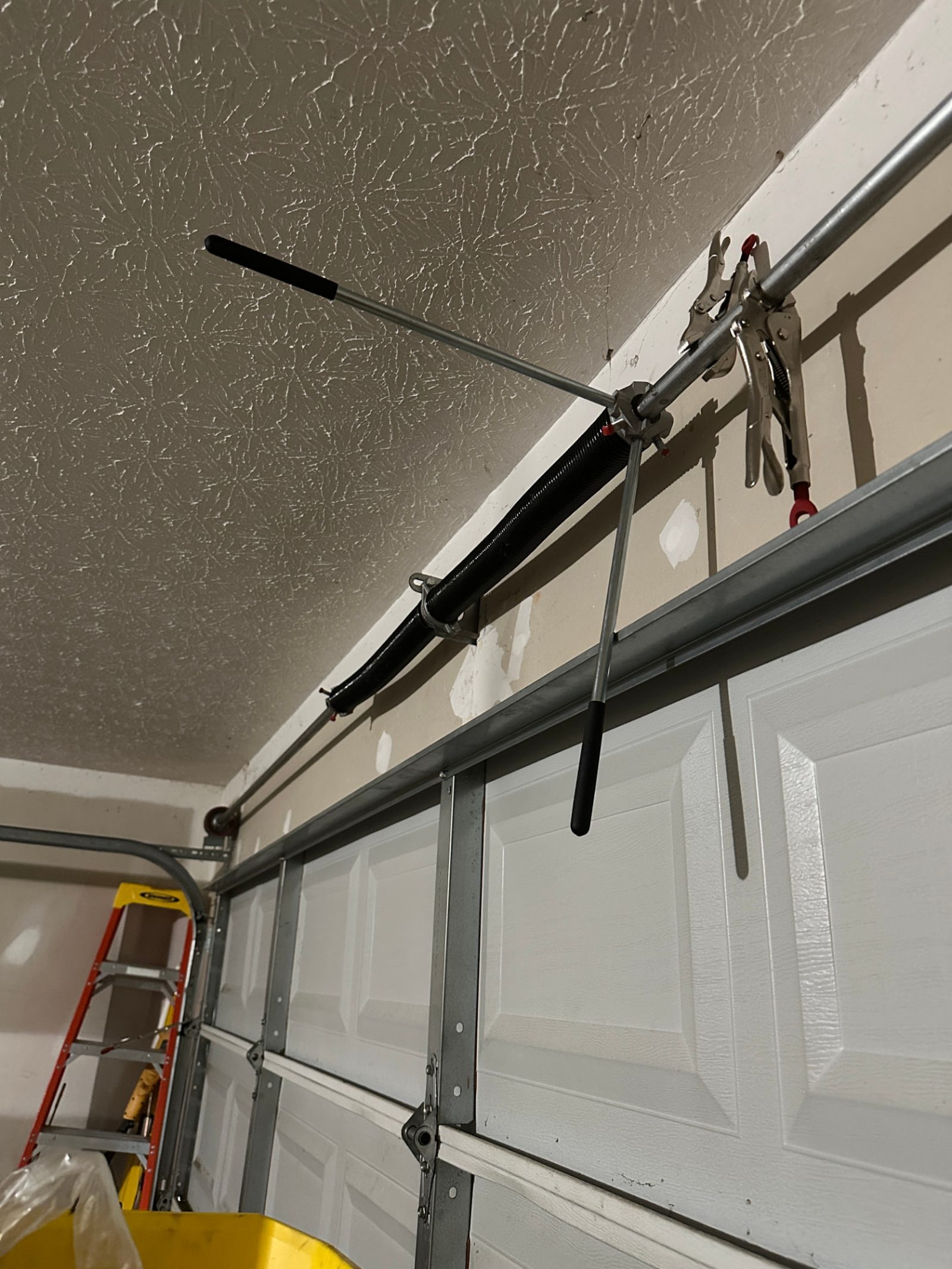 Technician servicing a garage door torsion spring to the correct tension with winding bars in Atlanta, Georgia