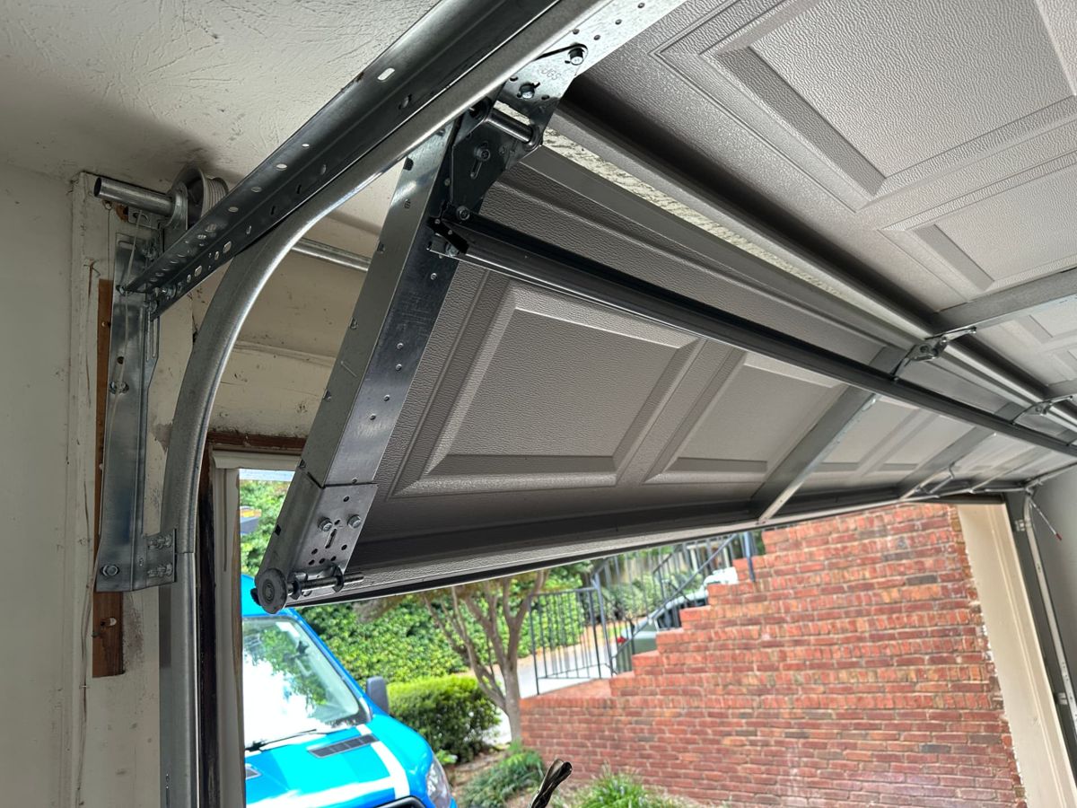 Garage door off its track and hanging unevenly, with the top section pulled away from the vertical track, in Tucker Georgia before repair